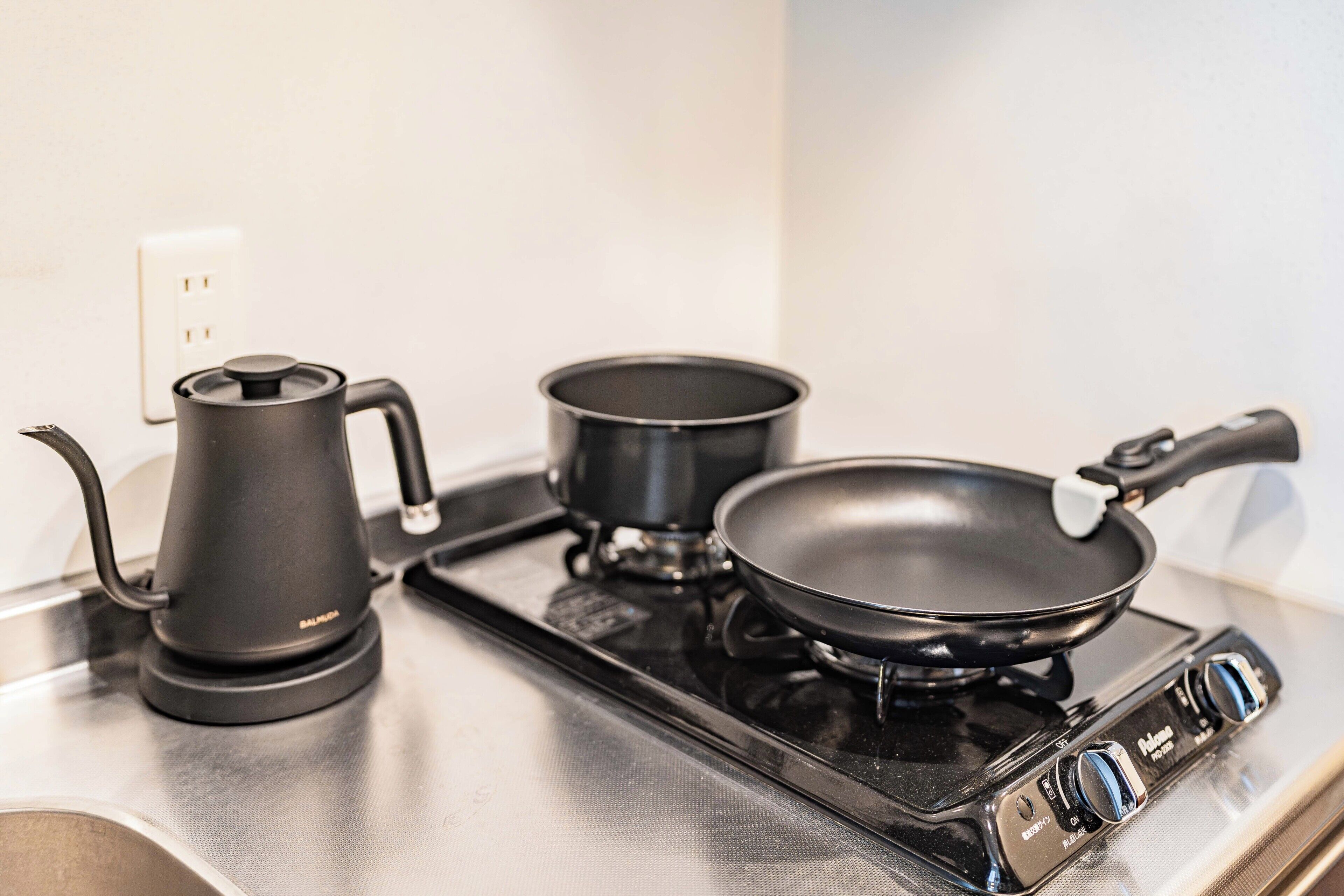 A kitchen with a stove, a kettle, and a frying pan.