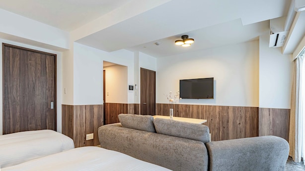 Camera d'albergo con due letti, un divano, una TV a schermo piatto e una parete decorativa in legno.