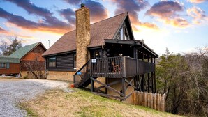A log cabin with a stone chimney, a wooden deck, and a porch. - Hot Tub + Game Loft | Located in Douglas Lake Resort | Mountains are Calling (Sevierville)