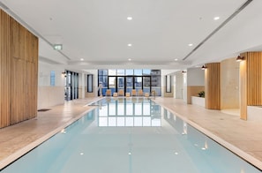 A modern indoor pool with clear glass walls, wooden paneling, and a view of the cityscape.
