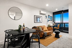 A modern living room with a round table, leather sofa, and a large window with a city view.