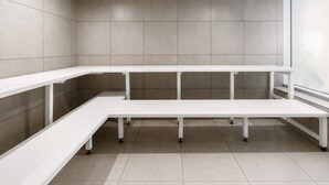 A modern, empty room with a long white bench, tiled walls, and a window.
