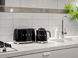 Une cuisine moderne équipée de deux appareils électroménagers noirs de la marque Smeg, d’un évier blanc et d’un robinet en acier inoxydable.