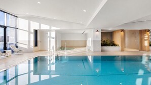 An indoor swimming pool with clear water, surrounded by white walls and a ceiling with recessed lighting.