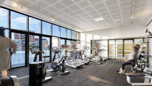 A gym with cardio machines, weight stations, and a large window offering a city view.