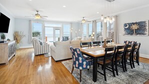 A spacious living room with a wooden floor, a dining area with a wooden table and chairs, and a ceiling fan. - Oceanfront w/ Pool, Panoramic Deck Views, 5BDR | Folly Ocean Breeze by AvantStay (Folly Beach)