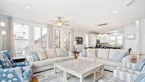 A spacious living area with a large sectional sofa, a coffee table, and a view of the kitchen. - Oceanfront w/ Pool, Panoramic Deck Views, 5BDR | Folly Ocean Breeze by AvantStay (Folly Beach)