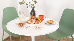 A round white table with a bowl of donuts and a red mug.