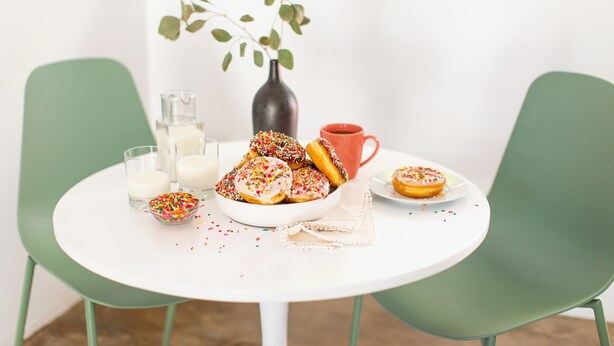 Een ronde witte tafel met een schaal donuts en een rode mok.