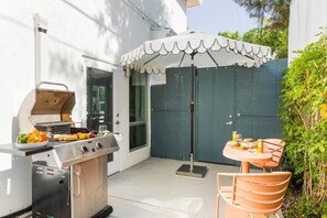 An outdoor patio with a grill, a table with chairs, and an umbrella.