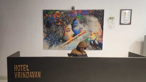 A hotel reception desk with a large mural of a mythological scene, a framed certificate on the wall, and a shelf with various items. - Hotel Vrindavan (Unnao)