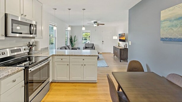 A modern kitchen with white cabinets, a built-in oven, and a microwave. There is a dining area with a table and chairs. - Sultan MAIN · Metro | Location | Convenience | Budget | 3 queen (Capitol Heights)