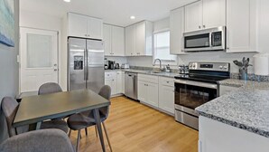 A modern kitchen with white cabinets, stainless steel appliances, a granite countertop, and a dining area with a table and chairs. - Sultan MAIN · Metro | Location | Convenience | Budget | 3 queen (Capitol Heights)