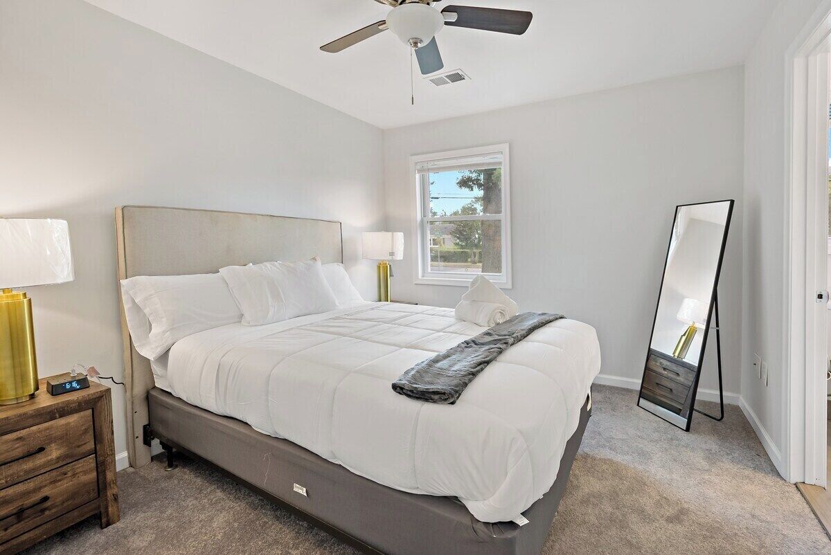 A bedroom with a bed, bedside tables, a ceiling fan, a window, and a mirror.