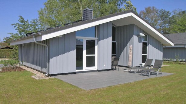 Une maison moderne de plain-pied, dotée d’un toit plat, de grandes portes-fenêtres coulissantes et d’un patio aménagé avec du mobilier d’extérieur.
