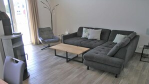Un salon moderne avec un canapé gris, une table basse en bois, un fauteuil gris et un grand lampadaire.