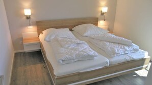 Un lit double avec une literie blanche et deux tables de chevet équipées de lampes fixées au mur.