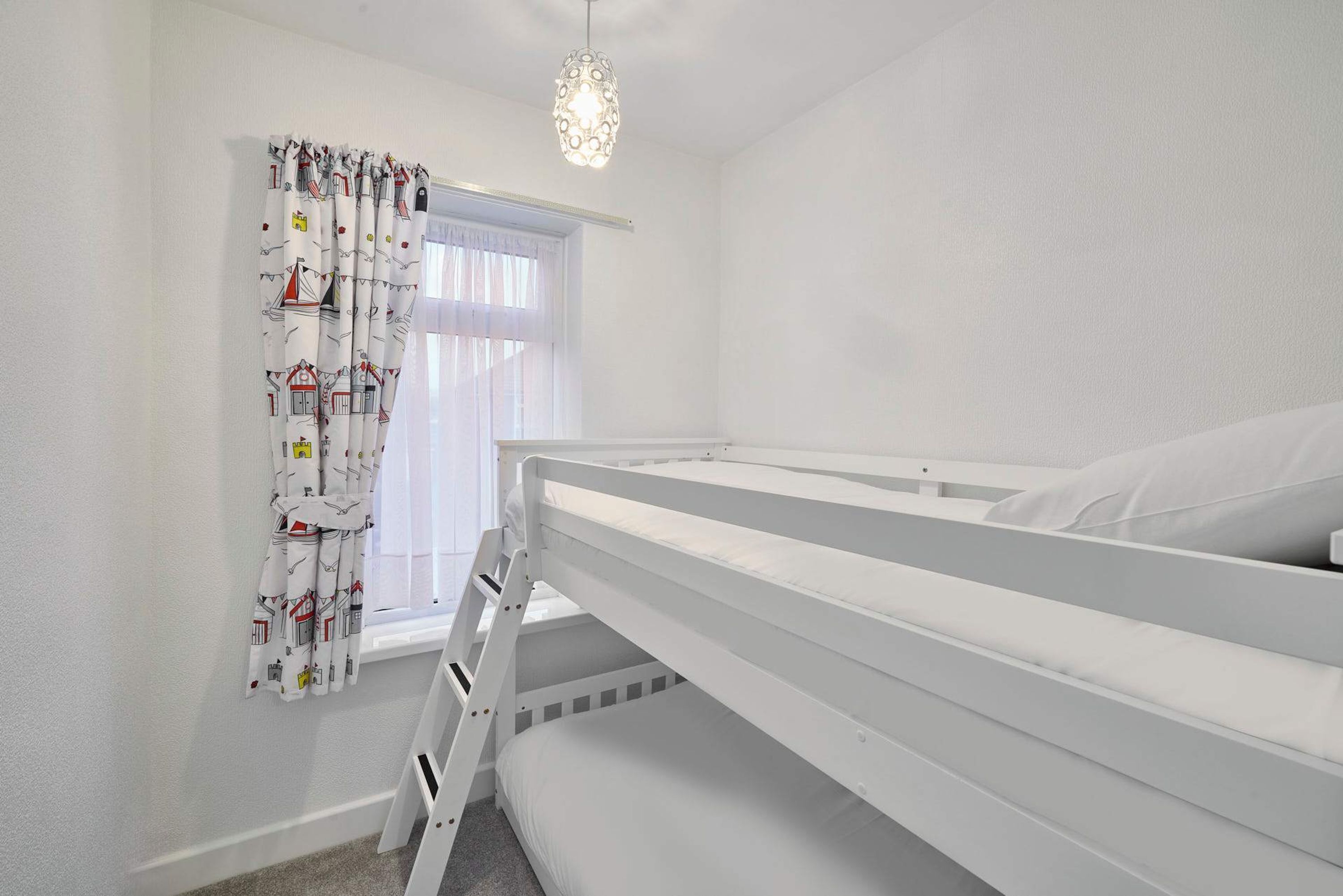 Une chambre avec un lit superposé, une fenêtre, des rideaux et un luminaire suspendu.