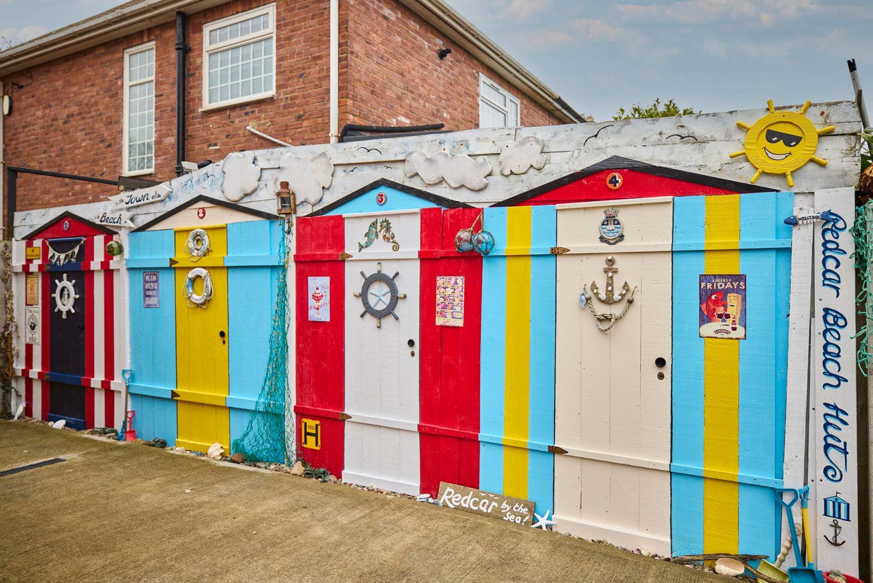 Una hilera de cabañas de playa coloridas con detalles náuticos y señalización.