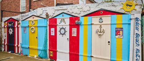 Una hilera de cabañas de playa coloridas con detalles náuticos y señalización.