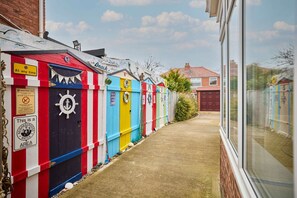 Une rangée de cabanes de plage aux couleurs vives, avec un chemin dégagé menant à une maison.