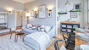 Un salon moderne avec un canapé gris, une table basse et un coin repas comprenant une table en bois mise pour deux personnes.