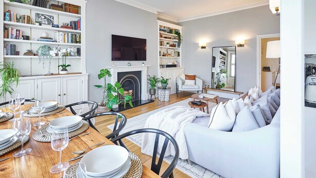 Un salon moderne avec une cheminée, un coin repas avec une table en bois dressée pour quatre personnes et un canapé blanc.