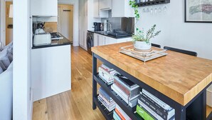 Une cuisine moderne avec des meubles blancs, une table à manger en bois et une bibliothèque remplie de livres.