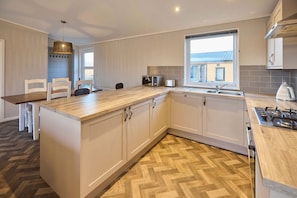 A modern kitchen with a central island, white cabinetry, and a herringbone wood floor. - Host Stay Hazelwood Deluxe Lodge (Hexham)