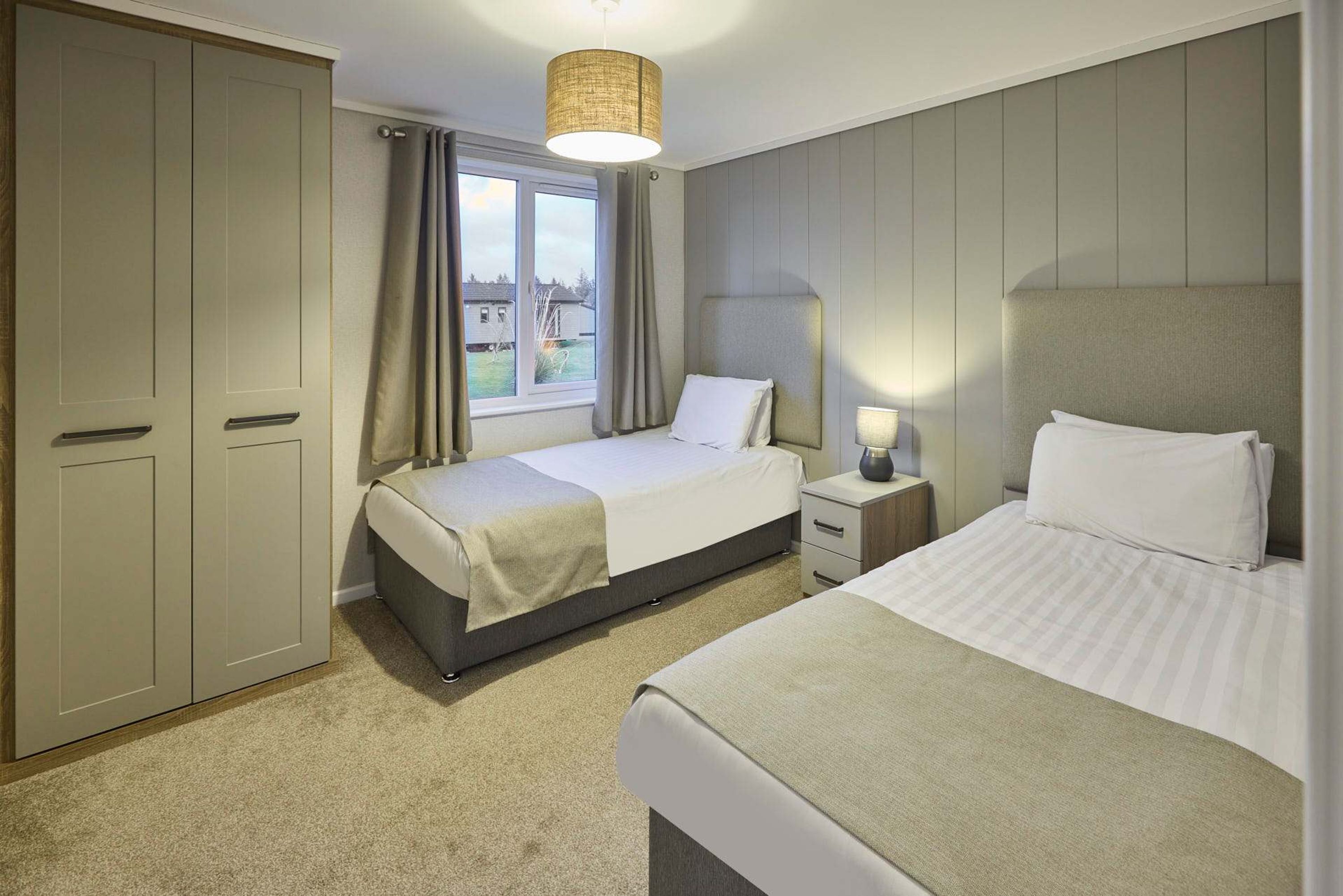 A hotel room with two beds, a wardrobe, a window with curtains, and a bedside lamp.
