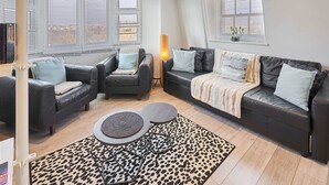 A modern living room with two black leather sofas, a small round table, and a leopard print rug. - Host Stay St James Street (Brighton)