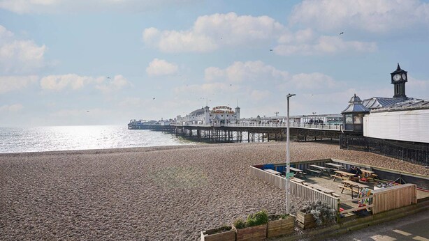 A pebbled beach with a pier extending into the sea, a clock tower, and a building labeled 'Brighton Pavilion'. - Host Stay St James Street (Brighton)