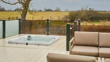 Ein Whirlpool auf einer Holzterrasse mit Blick auf ein Feld.