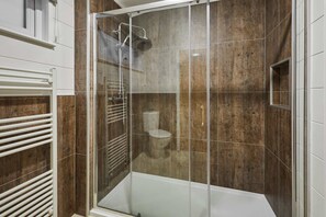 Een moderne badkamer met een douchecabine van glas, een witte badkuip en een houten wand.
