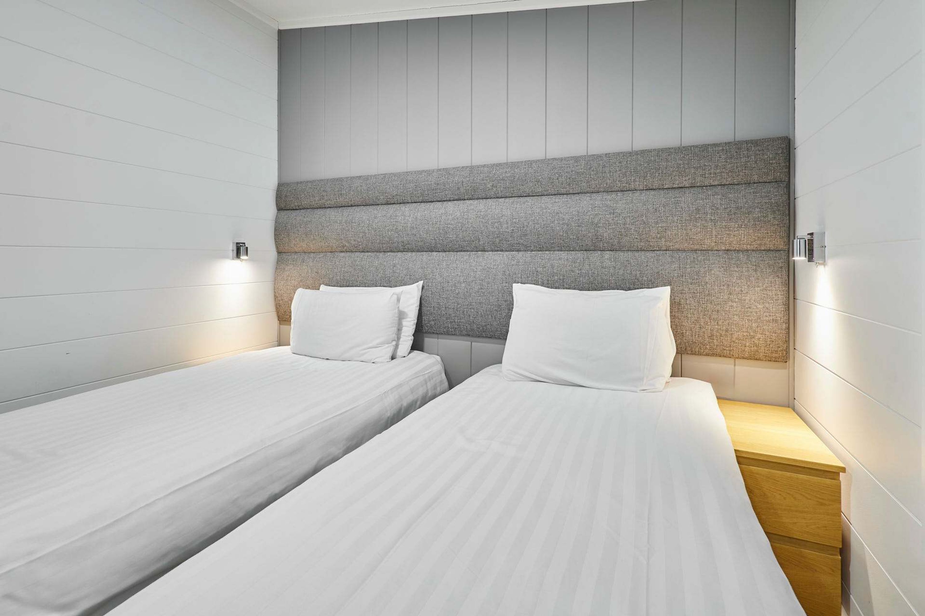 A hotel room with two single beds, a wooden nightstand, and a headboard with a grey panel.