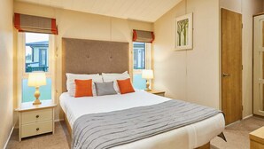 A bedroom with a large bed, two bedside tables with lamps, a wooden door, and a window with a view of a building. - Host Stay Portland 1 (Hexham)