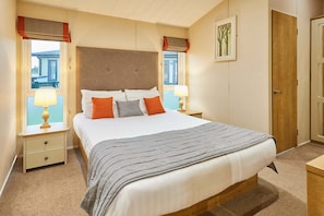 Une chambre à coucher avec un grand lit, deux tables de chevet avec des lampes, une porte en bois et une fenêtre donnant sur un immeuble.