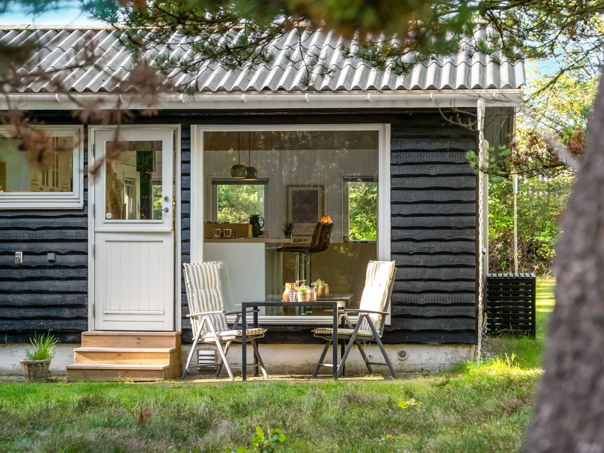 Una piccola baita con una porta vetrata scorrevole, un patio in legno e due sedie.