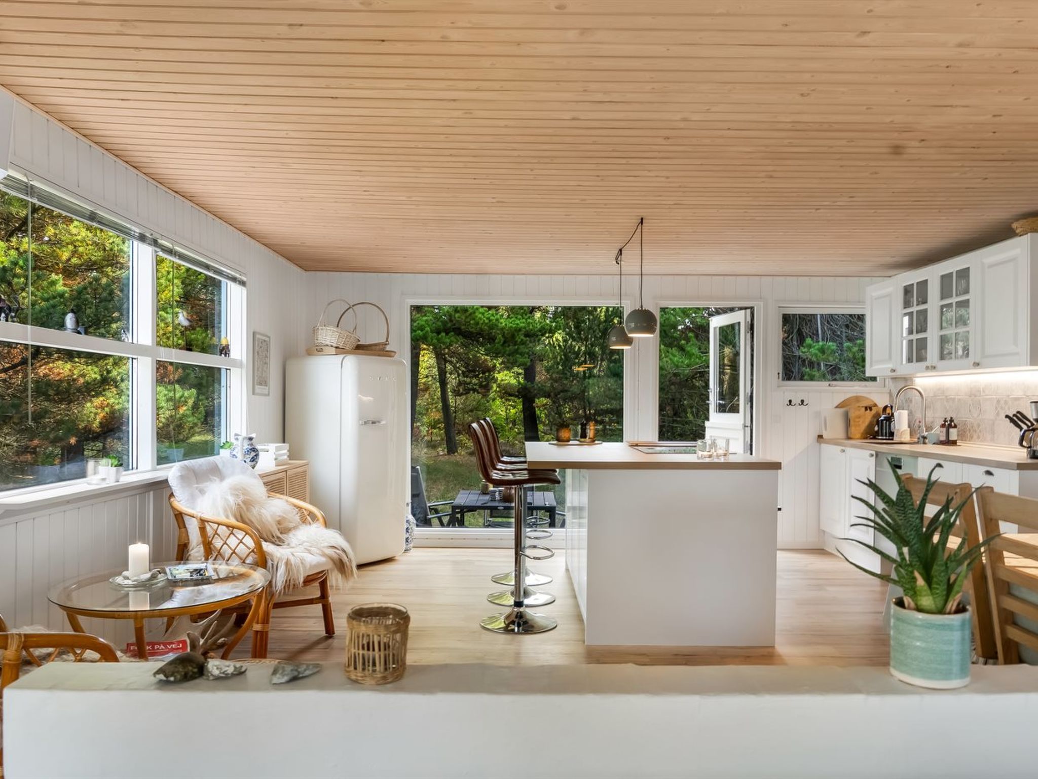 A modern kitchen with a central island, white cabinetry, and large windows offering a view of the outdoors.