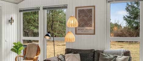 A room with a grey sofa, a wicker chair, a coffee table with a bottle and glasses, and a framed picture on the wall.