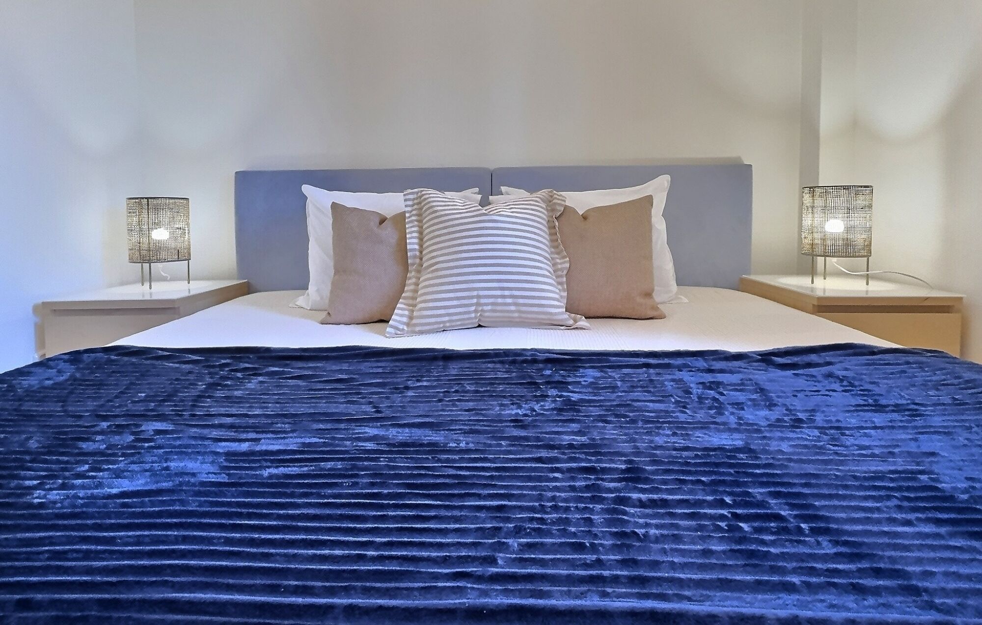Un lit recouvert d’une couverture bleu foncé, avec des oreillers blancs et deux tables de chevet dotées de lampes.