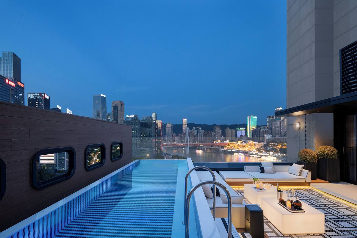 Een zwembad op het dak met uitzicht over de stad, modern buitengemeubilair en een poolbar.