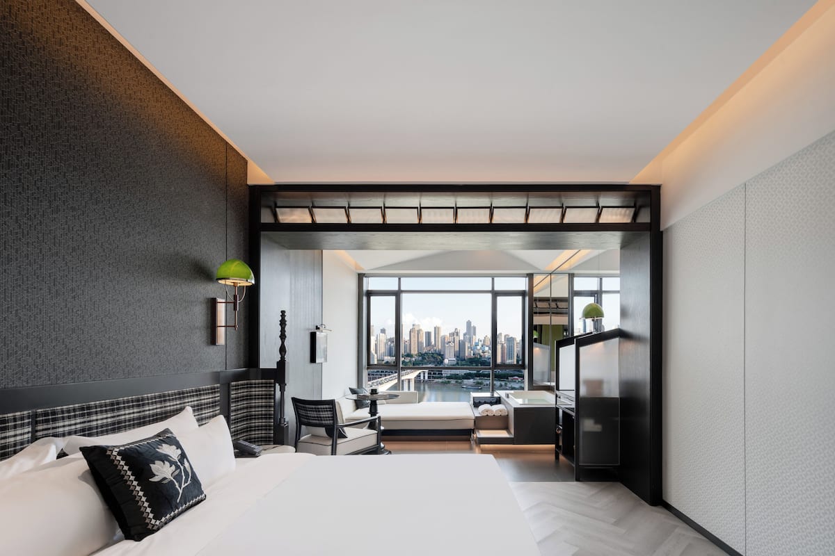 Een moderne hotelkamer met een groot bed, een zithoek, uitzicht op de stad en een kitchenette.