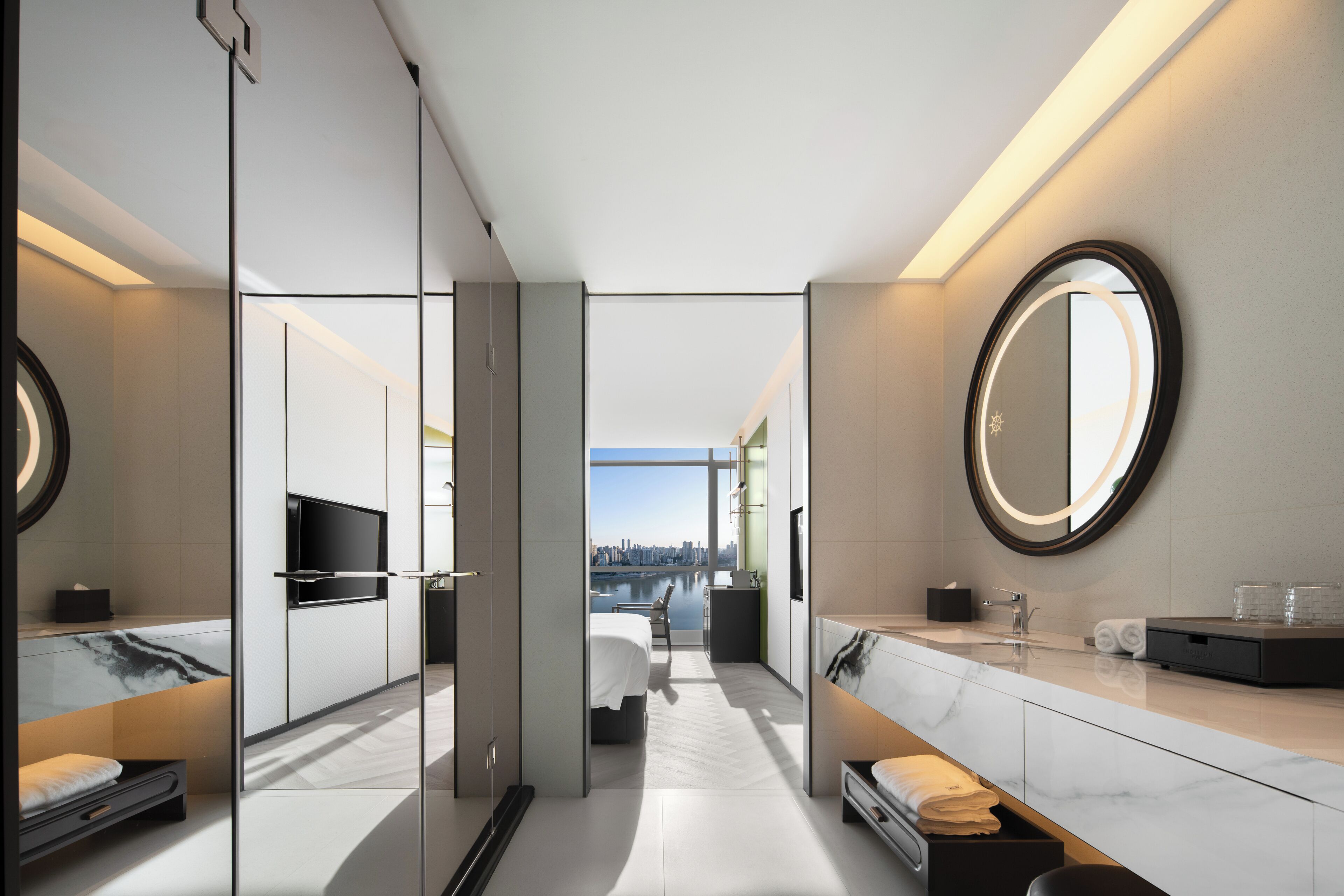 A modern hotel room with a large bed, a bathroom with a vanity, and a city view.