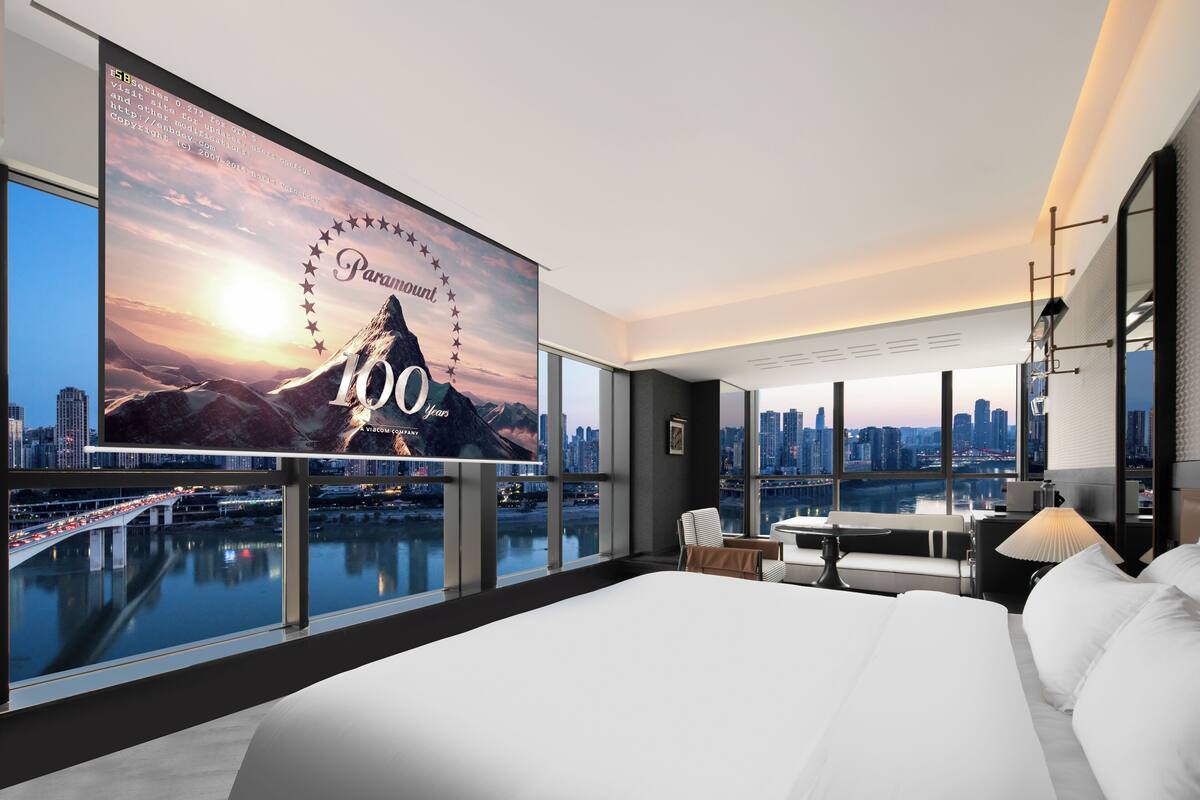 Een moderne hotelkamer met een groot bed, een bureau en uitzicht op een stadshemel en een rivier.