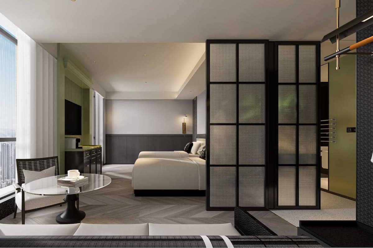 Een moderne hotelkamer met een groot bed, een ronde eettafel en uitzicht op de stad door grote ramen.