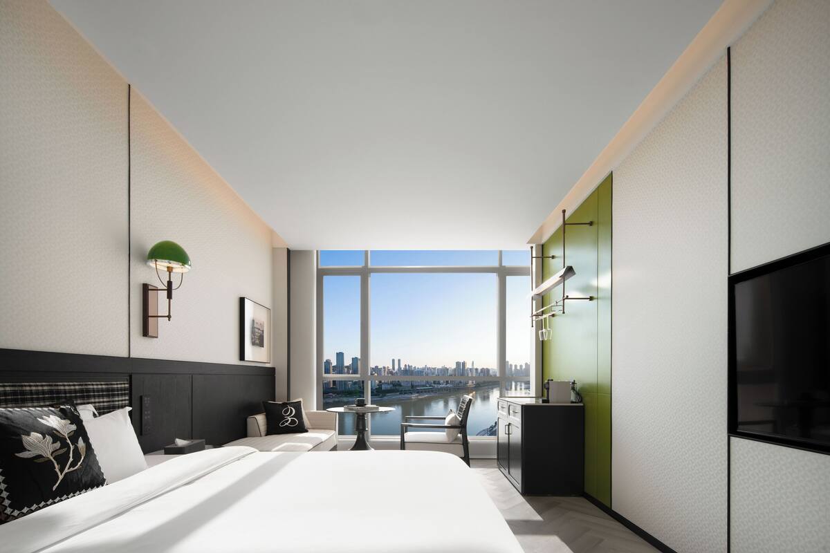 Een moderne hotelkamer met een groot bed, een bureau, een stoel, een televisie en uitzicht op een stadshemelbeeld.
