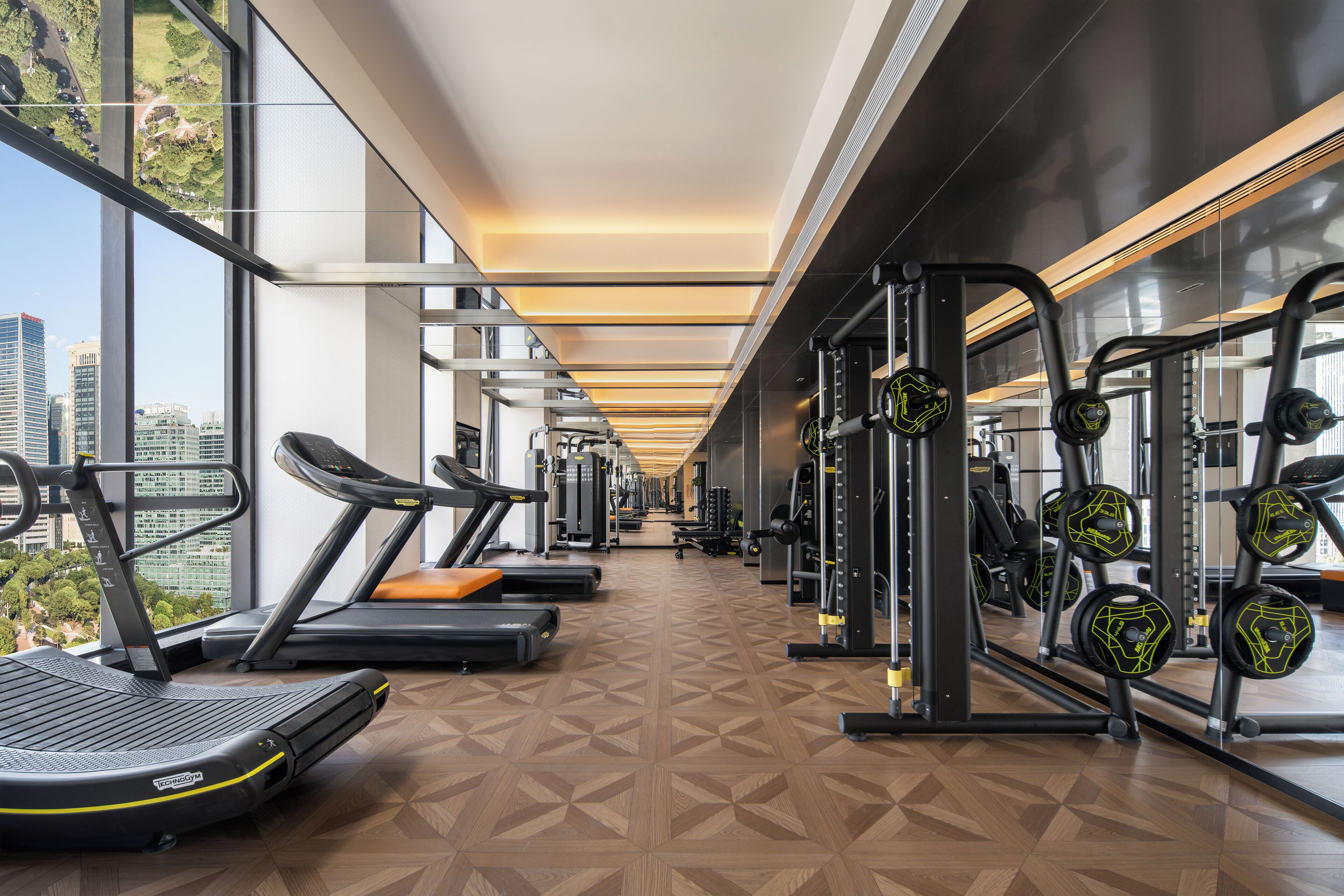 A gym with treadmills, weight machines, and a city view.