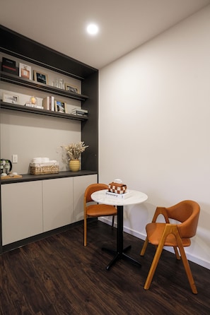 A modern kitchen with dark wood flooring, white cabinets, and a round table with two orange chairs. - Kiwuki Dalat Resort (Lang Biang - Da Lat)