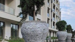 Un bâtiment moderne doté d’un bassin à eau miroir, de grands jardinières en pierre et surplombant un ciel dégagé.